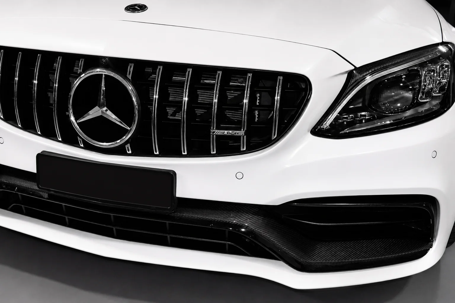 Close-up of a white Mercedes-AMG C-Class front grille and headlight
